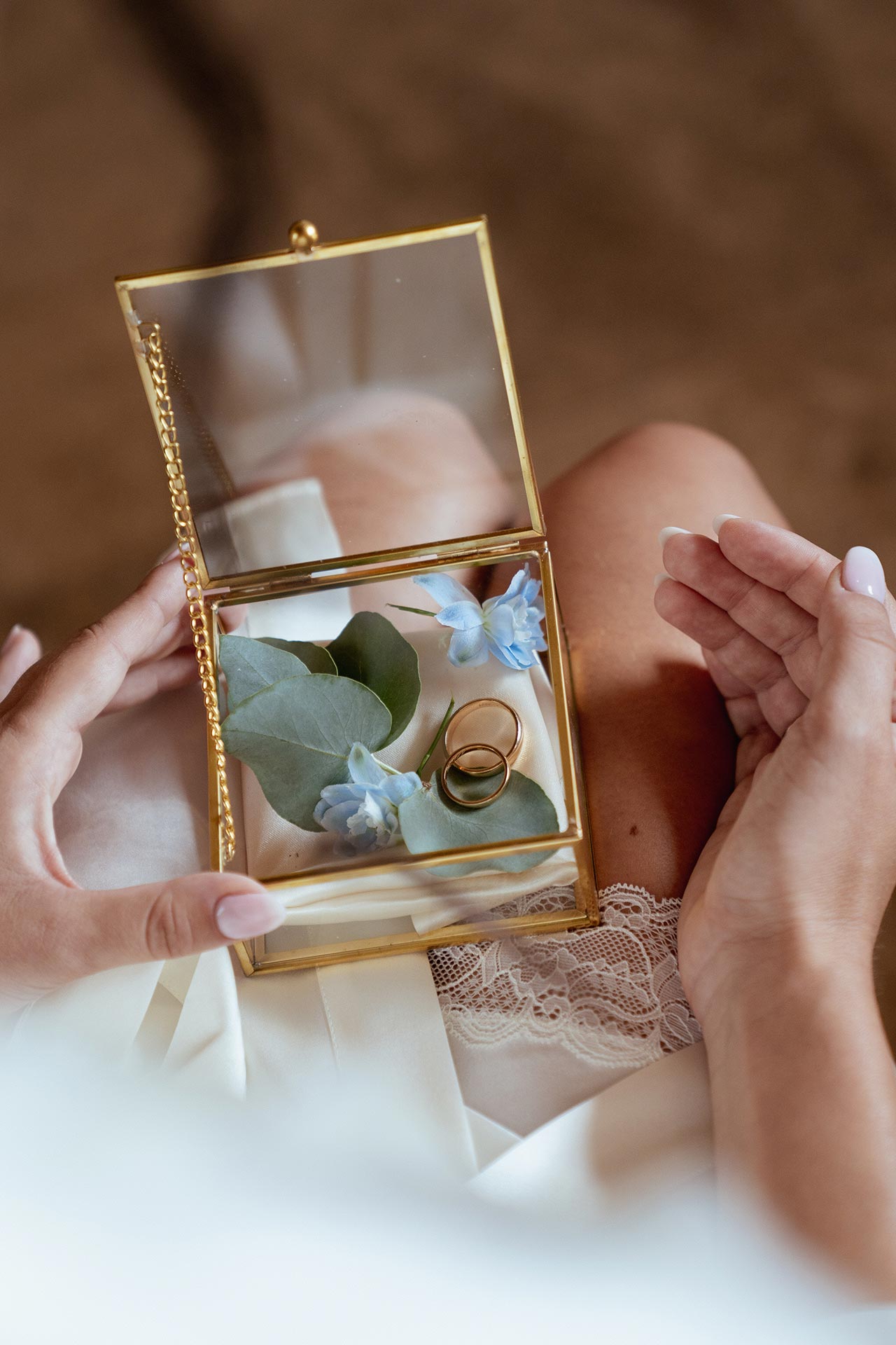 Fedi nuziali in oro in un cofanetto dorato con fiori azzurri ed eucalipto, pronte per la cerimonia di matrimonio